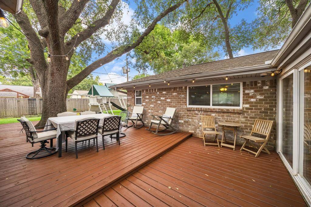 This photo showcases the charming backyard with a spacious wooden deck, perfect for entertaining. It features outdoor dining and seating areas under the shade of large trees, creating a cozy and inviting atmosphere.