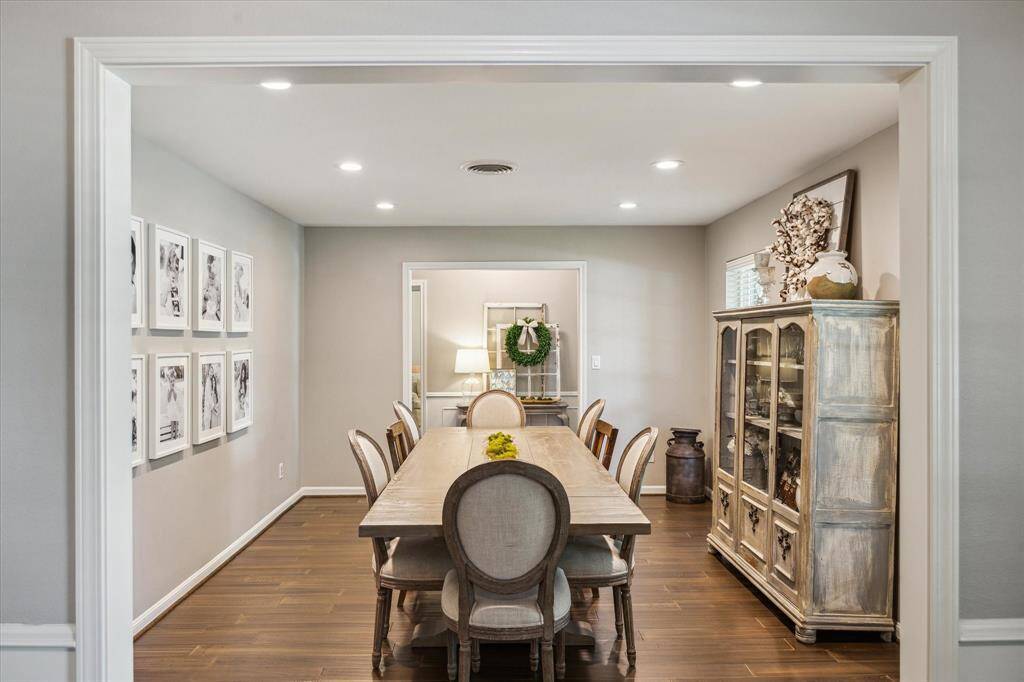 This photo showcases a stylish dining room with a long wooden table and elegant chairs. The room features hardwood flooring, recessed lighting, and tasteful wall decor. A vintage cabinet adds charm, while neutral tones create a warm, inviting atmosphere.