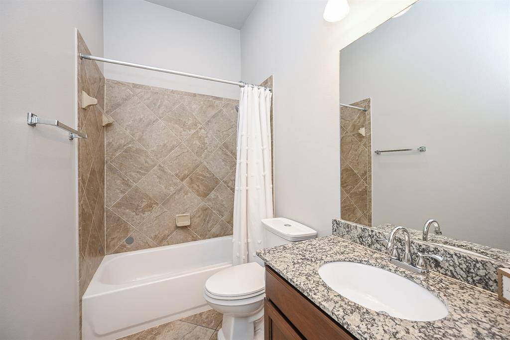Hall bath offers tub and shower, and vanity with sink. Beige tile coordinates beautifully with granite topped vanity.
