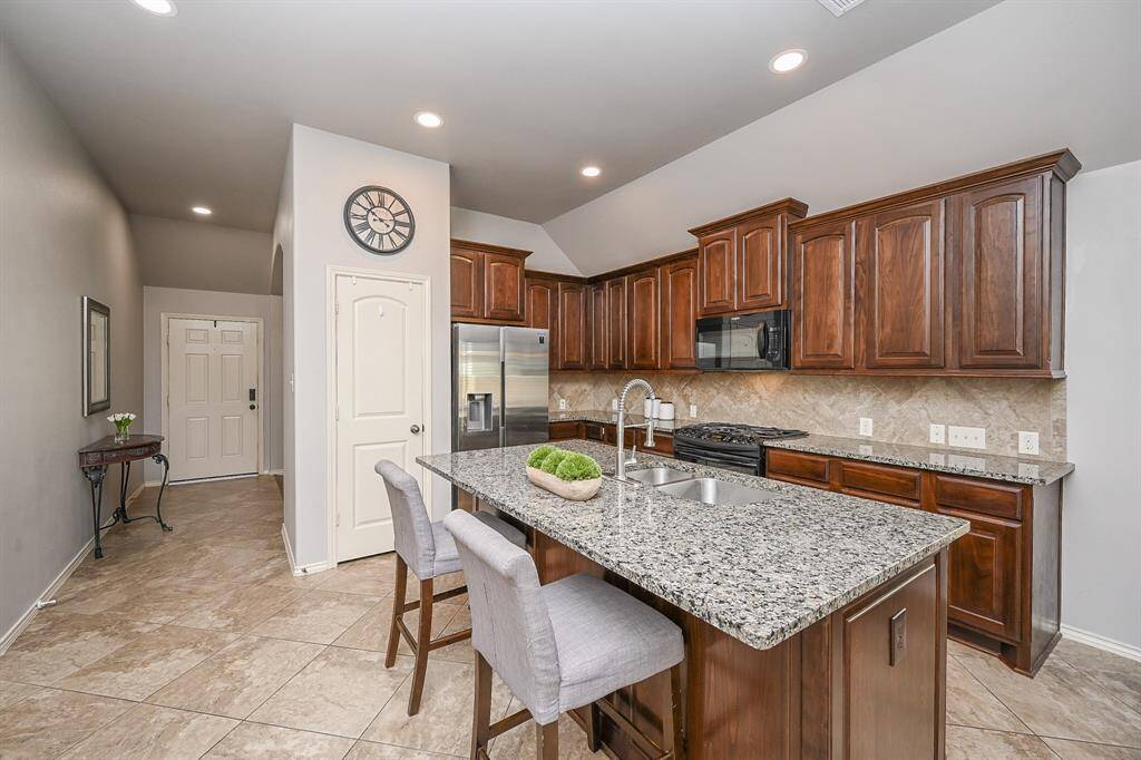 This photo showcases a spacious, modern kitchen and a large granite island. The open layout includes the great dining area with plenty of natural light from large windows. Neutral tile flooring complements the sleek design, creating a welcoming space