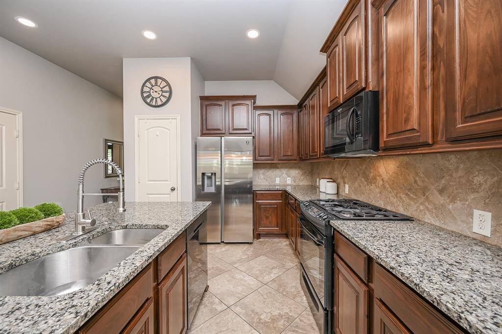 This kitchen features sleek granite countertops, rich wood cabinetry, and modern stainless steel appliances. It includes an island with seating perfect for entertaining, snacks, lunch, or dinner. Wood cabinetry creates a warm and inviting space.