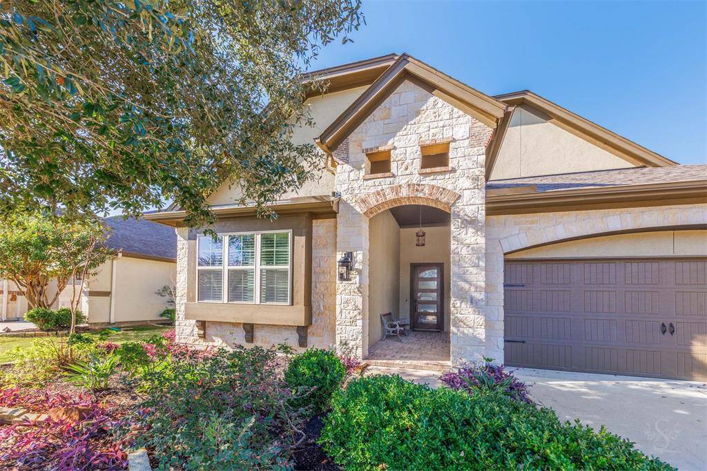 A close up of the the arched stone entryway and covered front porch create a warm and inviting arrival. Gorgeous lush landscaping highlights the home's thoughtful design and serene vibe. Recent exterior paint and foam insulation added - “cooler” attic storage.