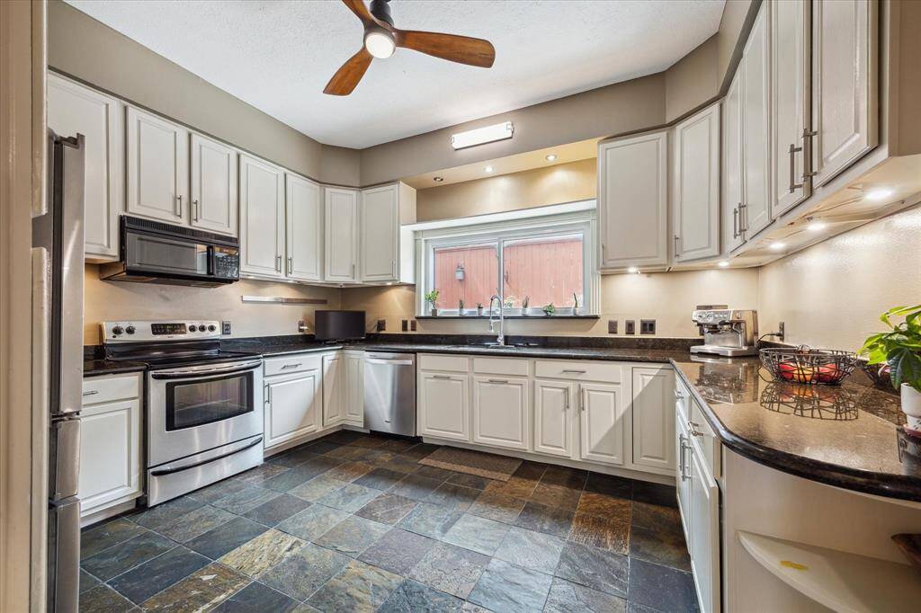 Rear House: Kitchen features modern stainless steel appliances, white cabinetry, and sleek black countertops. A ceiling fan and under-cabinet lighting enhance the space, while a large window provides natural light. The dark, textured floor adds a touch of elegance.