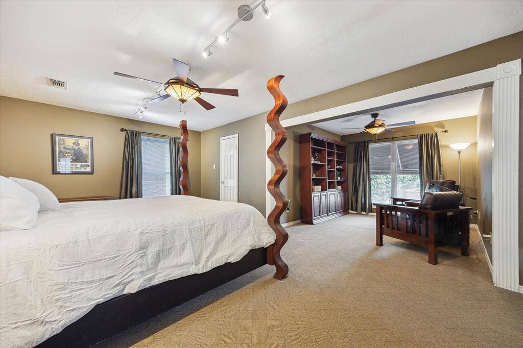 Rear House: Spacious primary bedroom features a cozy sitting area with built-in shelves, stylish ceiling fans, and abundant natural light from large windows. The room has a warm, inviting atmosphere with neutral tones and unique design elements.