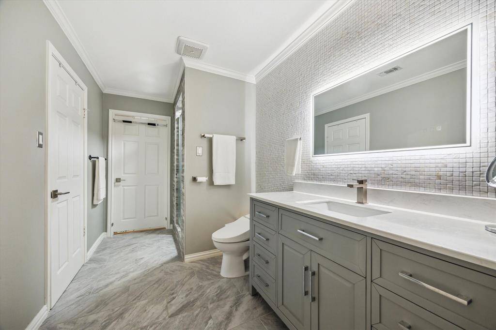 Rear House: This modern primary bathroom features a sleek vanity with ample storage, a large illuminated mirror, and elegant tiling. The neutral color palette and clean lines create a fresh and inviting space.