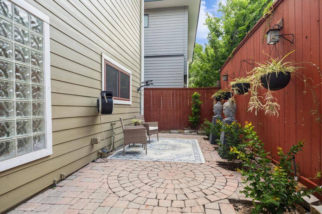 Rear House: Another view of this charming, private patio with brick pavers and a red wooden fence. Features include outdoor seating, hanging plants, and decorative urns, perfect for relaxation or entertaining.