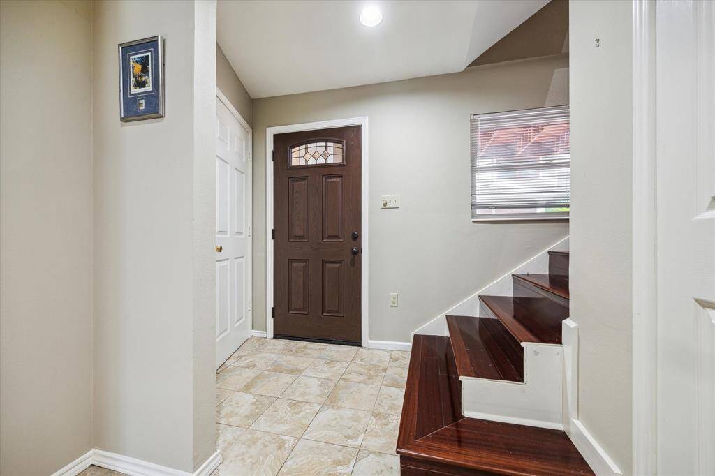 Front House:  Welcoming entryway with a dark wooden front door, tiled floor, and a staircase with wooden steps leading up. A small window provides natural light, and there is a closet door on the left, enhancing functionality.