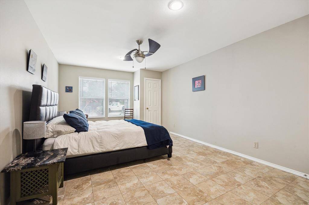 Front House: One of two spacious bedrooms features tiled flooring, neutral walls, and ample natural light from large windows.