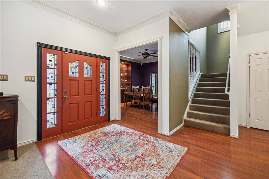 Rear House: Inviting entryway of  features a vibrant red door with stained glass panels, elegant hardwood flooring, and a decorative rug. The open layout leads to a formal dining area with wooden furniture and a staircase ascending to the upper level.