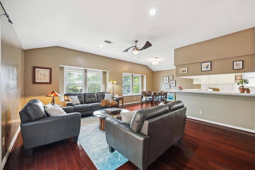 Front House: Another view of this inviting living room features hardwood floors, ample natural light from large windows, and an open layout connecting to a modern kitchen.