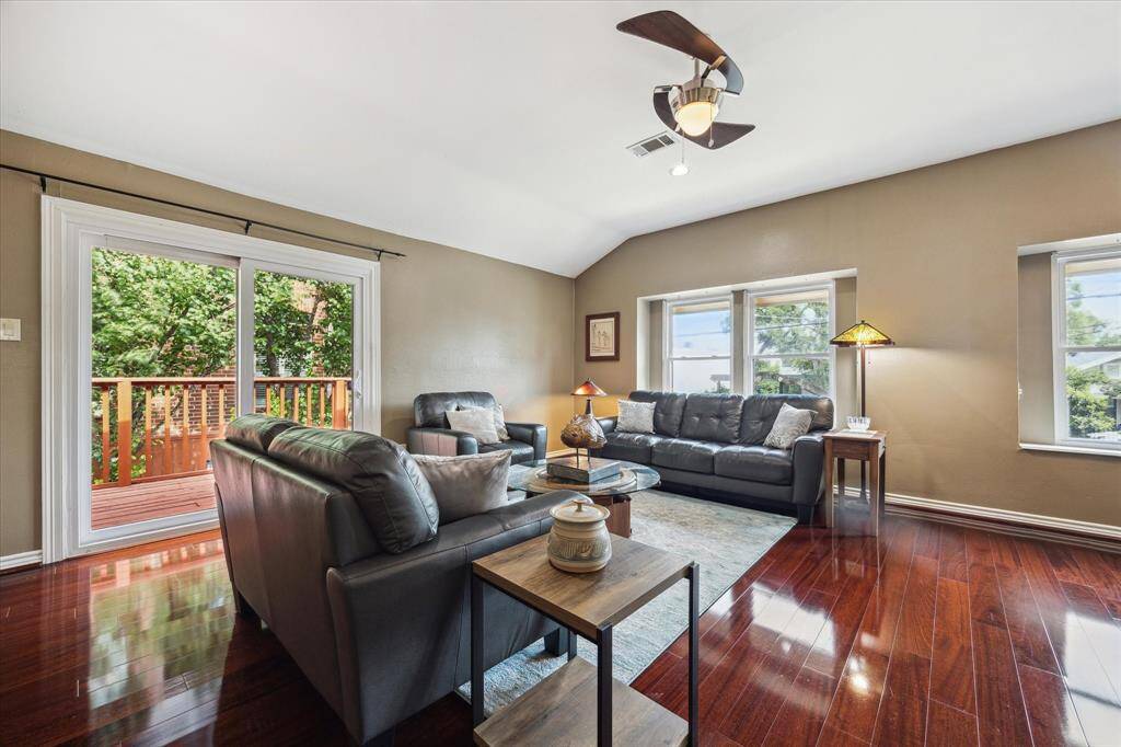Front House: Living room is spacious and bright, featuring polished hardwood floors and a vaulted ceiling. Ample natural light from large windows and sliding doors that open to a wooden deck.