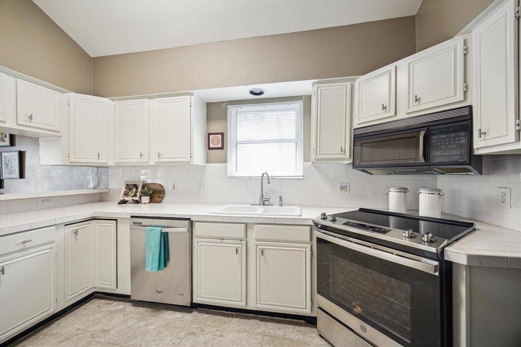 Front House: Kitchen features a modern design with white cabinetry, stainless steel appliances, and a sleek electric stove. The neutral color palette and tiled flooring enhance the clean, spacious feel.