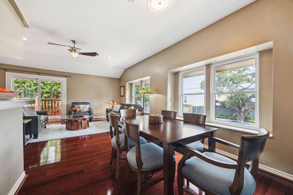 Front House: Open concept living and dining area with rich hardwood floors, ample natural light from large windows, and a cozy seating nook. A ceiling fan adds comfort, and sliding doors lead to an outdoor deck, perfect for entertaining.