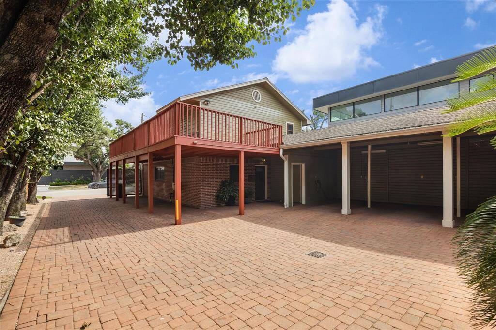 Spacious brick-paved driveway with a covered parking area and a wooden deck above. Enhanced by surrounding trees and a modern architectural design, offering both functionality and style.