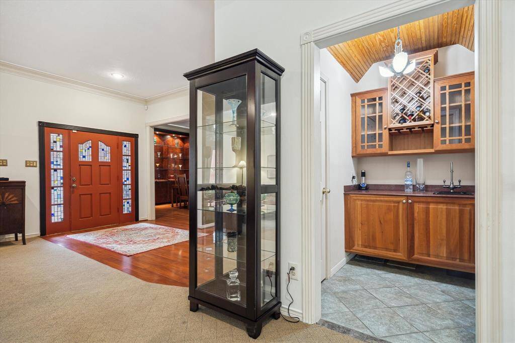 Rear House: Welcoming entryway with a stylish red door featuring decorative glass panels. Adjacent is a cozy wet bar area with wooden cabinetry and a wine rack. The space is accented by a glass display cabinet and hardwood flooring, creating an inviting atmosphere.
