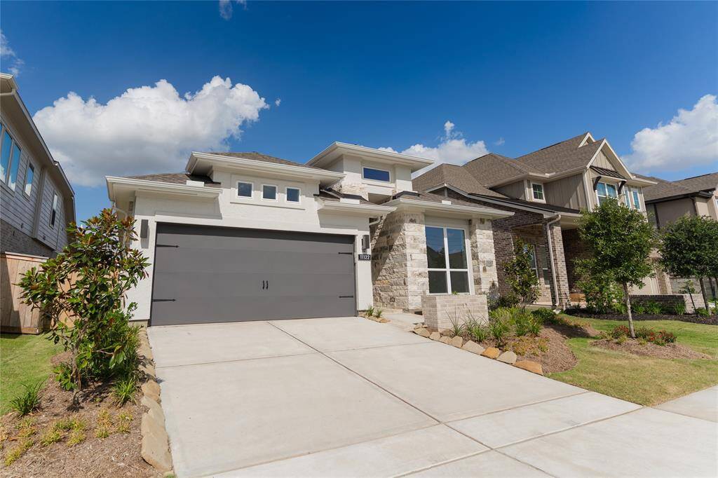 Modern two-story home with a sleek design featuring a spacious driveway and two-car garage. The exterior combines brick and stone accents, complemented by a well-maintained front yard with landscaping. Ideal for contemporary living in a suburban neighborhood.