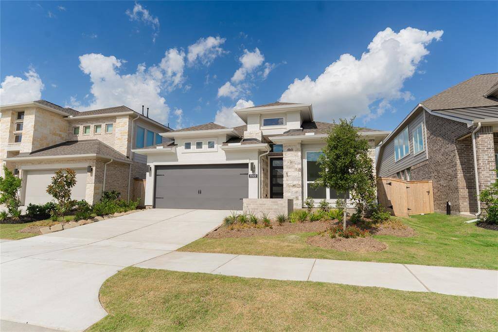 This modern home features a sleek exterior with a two-car garage, well-maintained landscaping, and a contemporary design. It's set in a neighborhood with similar homes and has a spacious driveway.