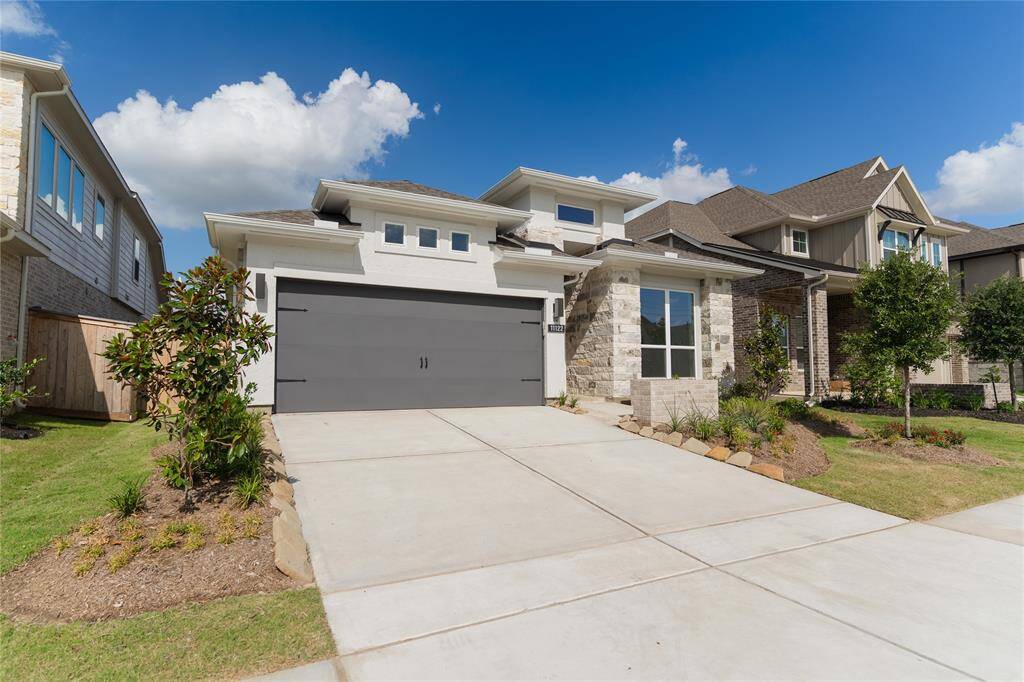 This is a modern two-story home with a sleek design featuring a stone and stucco exterior. It has a double garage, a well-maintained front yard, and is situated in a suburban neighborhood.