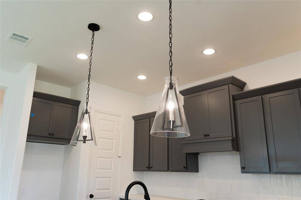 Modern kitchen with sleek dark cabinets and stylish pendant lighting. Features recessed lights, a clean white ceiling, and a contemporary door design.