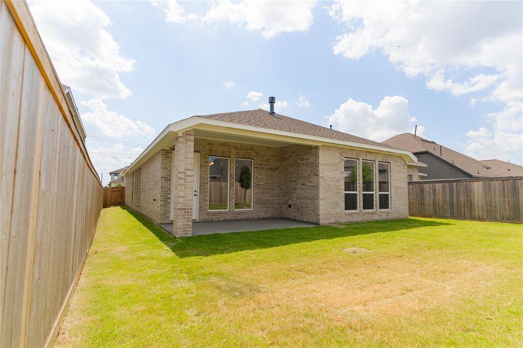 This photo showcases a brick home with a covered patio, located in a fenced backyard with a well-maintained lawn. Ideal for outdoor activities and privacy.