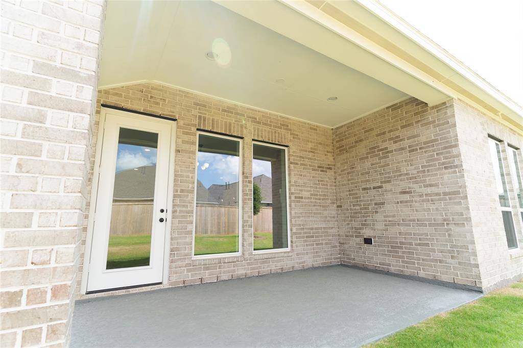 This photo showcases a covered patio with brick walls, featuring a white door flanked by large windows, opening to a grassy backyard. Ideal for outdoor relaxation.