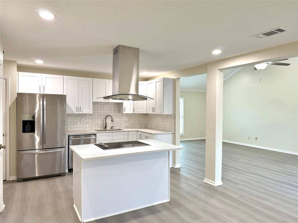 Welcome to 11127 Willwood, your future home showcasing a modern open-concept kitchen and living area. The kitchen features sleek stainless steel appliances, white Shaker-style cabinetry, quartz countertops, and a central island with a built-in cooktop—perfect for both everyday use and entertaining. Recessed lighting illuminates the space, which flows seamlessly into a spacious living area with luxury vinyl plank flooring and a welcoming atmosphere.