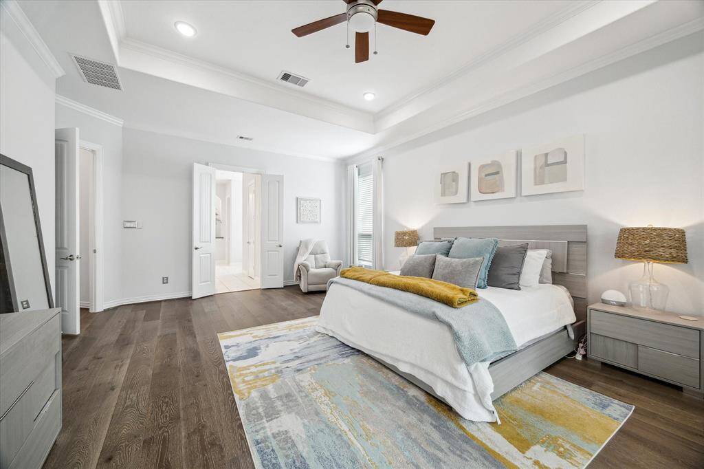 Double doors lead from the spacious bedroom into a private ensuite bath, creating a seamless transition between comfort and luxury. Soft wall tones, wide-plank flooring, and a tray ceiling with crown molding bring an elevated feel, while natural light and layered textures add warmth to the restful setting.