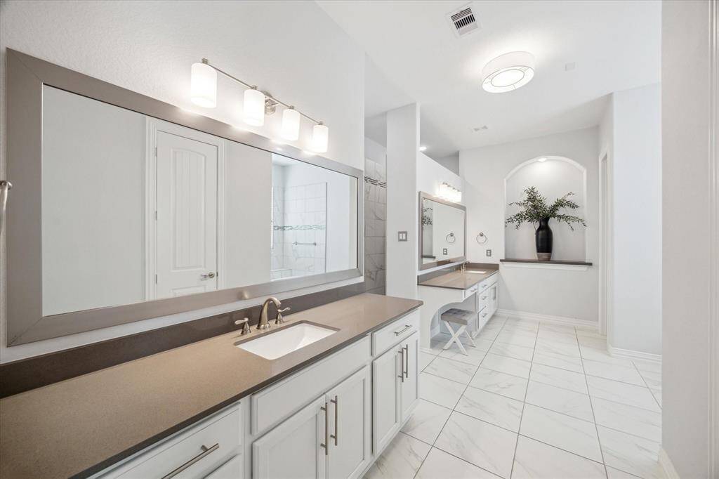 Refined finishes and thoughtful layout define this serene primary bath. Dual vanities with quartz countertops and framed mirrors provide ample space for daily routines, while a dedicated makeup station adds a luxurious touch. Polished tile floors, arched details, and soft lighting elevate the room's tranquil feel, creating a space that’s as functional as it is beautiful.