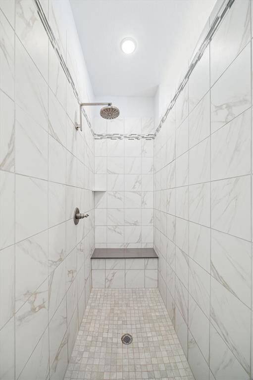 Designed for both comfort and style, this oversized walk-in shower features marble-look tile, a mosaic floor, and brushed-nickel fixtures. A built-in bench offers convenience, while the rainfall showerhead adds a spa-inspired touch to the daily routine.