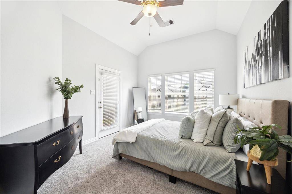 Vaulted ceilings and multiple windows create an airy atmosphere in this upstairs secondary bedroom. Soft carpeting adds comfort underfoot, while the glass door provides direct access to the upstairs balcony—making this space feel both spacious and connected to the outdoors.