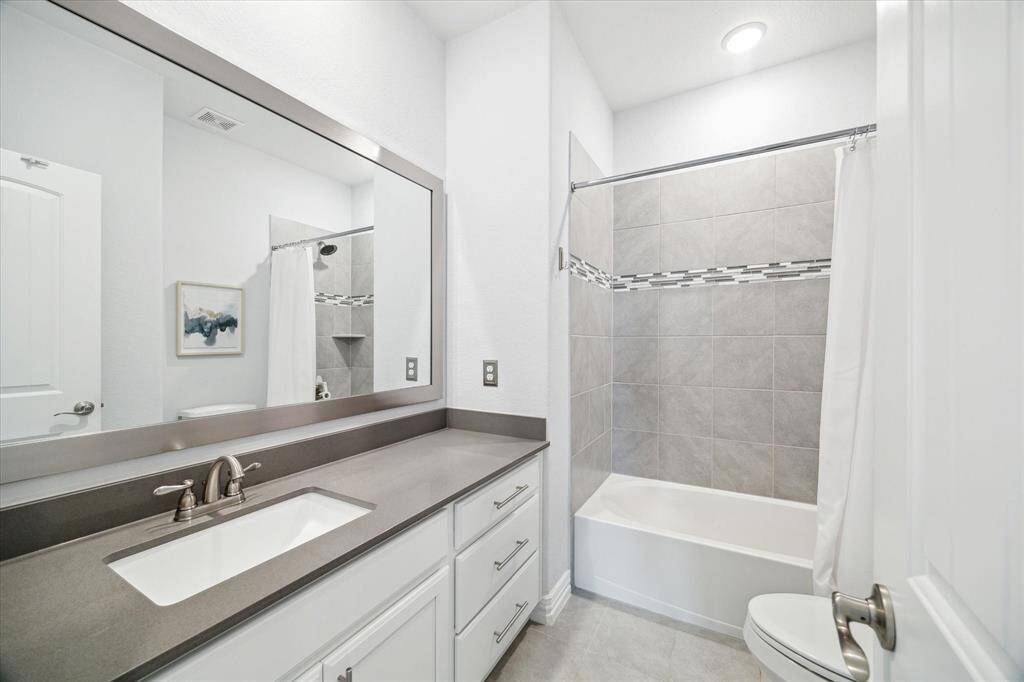 This ensuite bathroom features a neutral palette and timeless materials, including a quartz countertop, undermount sink, and a spacious tub with full tile surround and mosaic accent trim. Polished and functional, it offers a private and comfortable retreat for guests or family members.