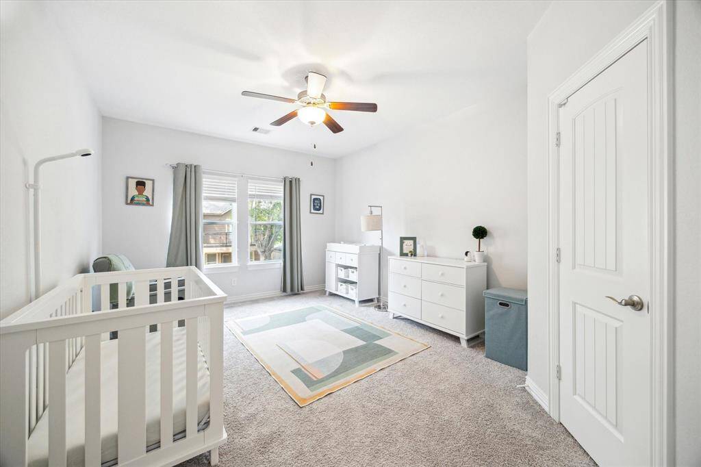 Soft tones and natural light create a soothing atmosphere in this versatile secondary bedroom. Currently used as a nursery, the space features plush carpeting, generous proportions, and large windows overlooking the front yard. Neutral finishes make it easy to reimagine as a guest room, home office, or playroom.