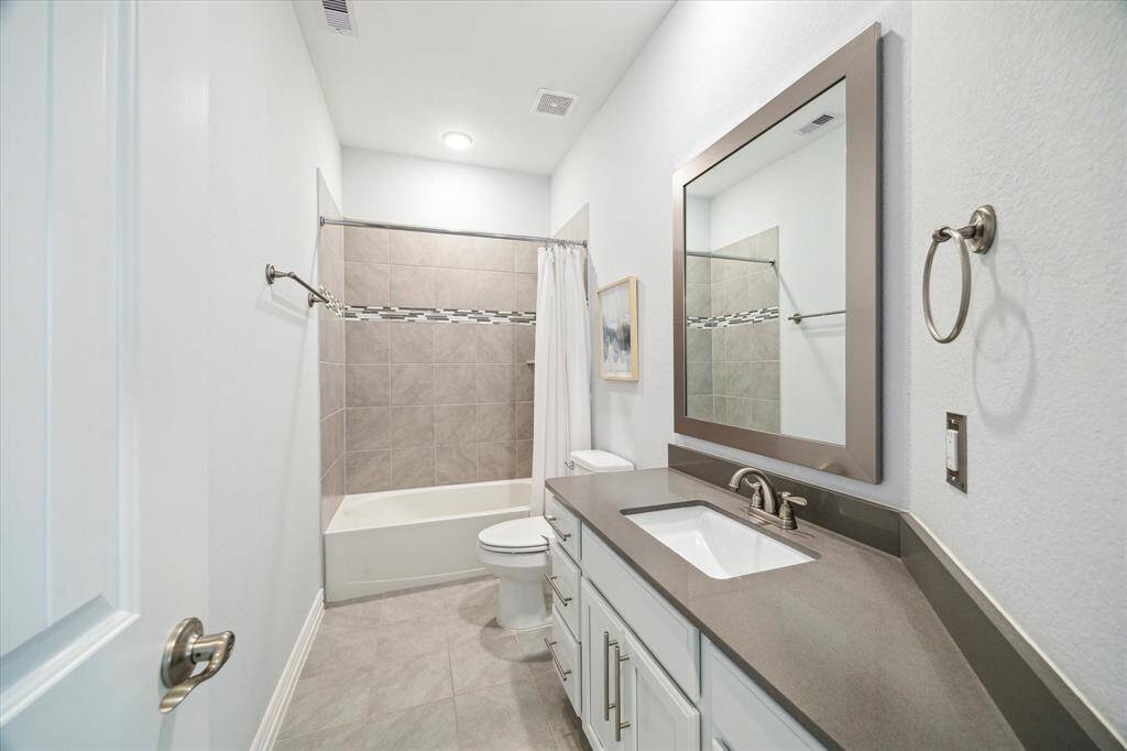 Crisp finishes and neutral tones define this well-appointed secondary bathroom. A quartz countertop, framed mirror, and brushed-nickel hardware bring contemporary appeal, while the tub/shower combo is surrounded by large-format tile and a mosaic accent band. Perfectly positioned to serve adjacent bedrooms or guests.