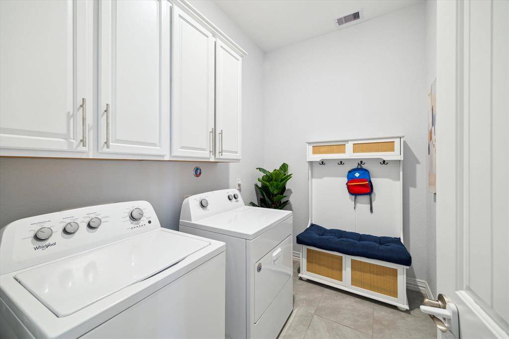 Combining practicality with thoughtful design, this laundry room features upper cabinetry for added storage, durable tile flooring, and a built-in bench with hooks—ideal for backpacks, jackets, or shoes. Conveniently located, this space helps keep the daily routine organized and streamlined.