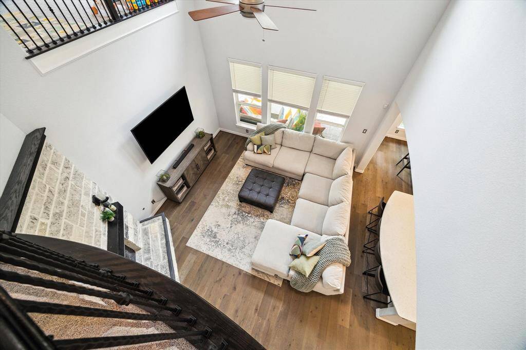 From above, the living room’s open-concept design shines—highlighting the soaring ceilings, statement fireplace, and seamless flow to the adjacent kitchen. Natural light pours in through a wall of windows, illuminating the spacious layout ideal for both everyday living and effortless entertaining. Rich wood flooring adds warmth and continuity throughout the main level.