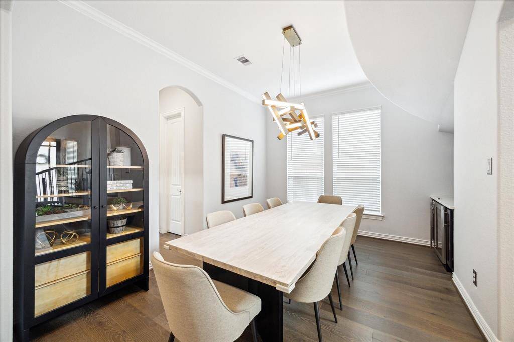 The formal dining room blends clean lines with contemporary design, featuring a statement light fixture, expansive windows that flood the space with natural light, and rich wood flooring that adds warmth and depth. A built-in beverage center provides added convenience for entertaining, while the arched doorways and high ceilings elevate the room’s architectural appeal.