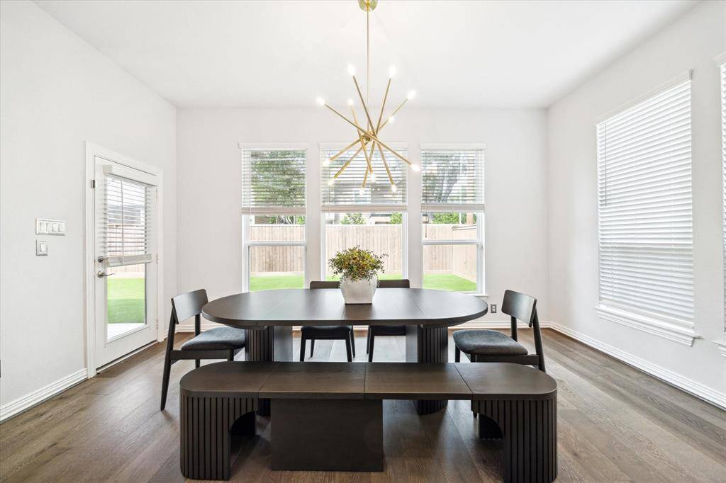Abundant natural light fills this casual dining space, where oversized windows overlook the backyard and create a bright, welcoming ambiance. A modern chandelier adds a touch of drama, while the open layout connects seamlessly to the kitchen and patio—ideal for both quiet mornings and effortless entertaining.