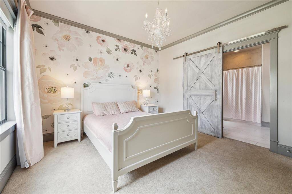 Secondary bedroom with whimsical wallpaper, carpet floor and barn door leading to large en-suite bathroom