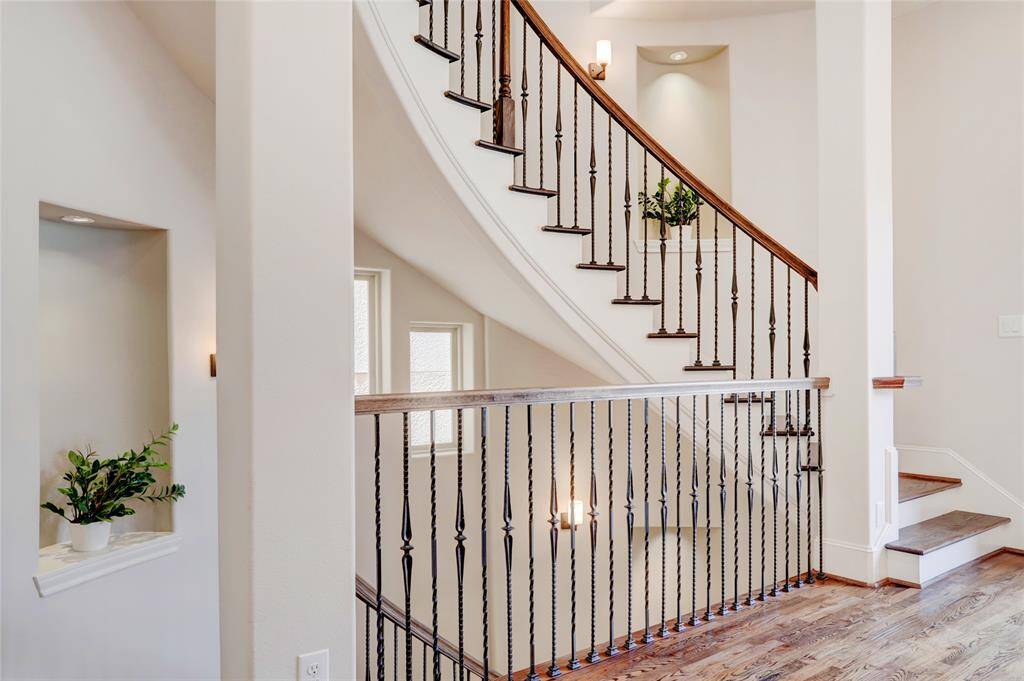 Another view of curved stair case with lighted art niches, wrought iron spindles, and wall scones that illuminate the space.