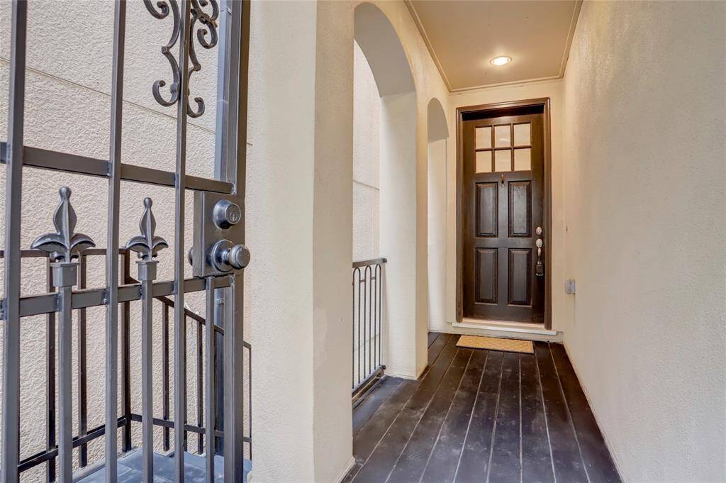 Private wrought iron gate entry porch leading to rich wood stained front door with divided glass on top panel. Notice the soft curved arches along the side of porch area.