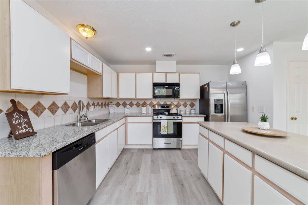 This kitchen features modern stainless-steel appliances, granite countertops, and a spacious island. White cabinetry and a tiled backsplash.