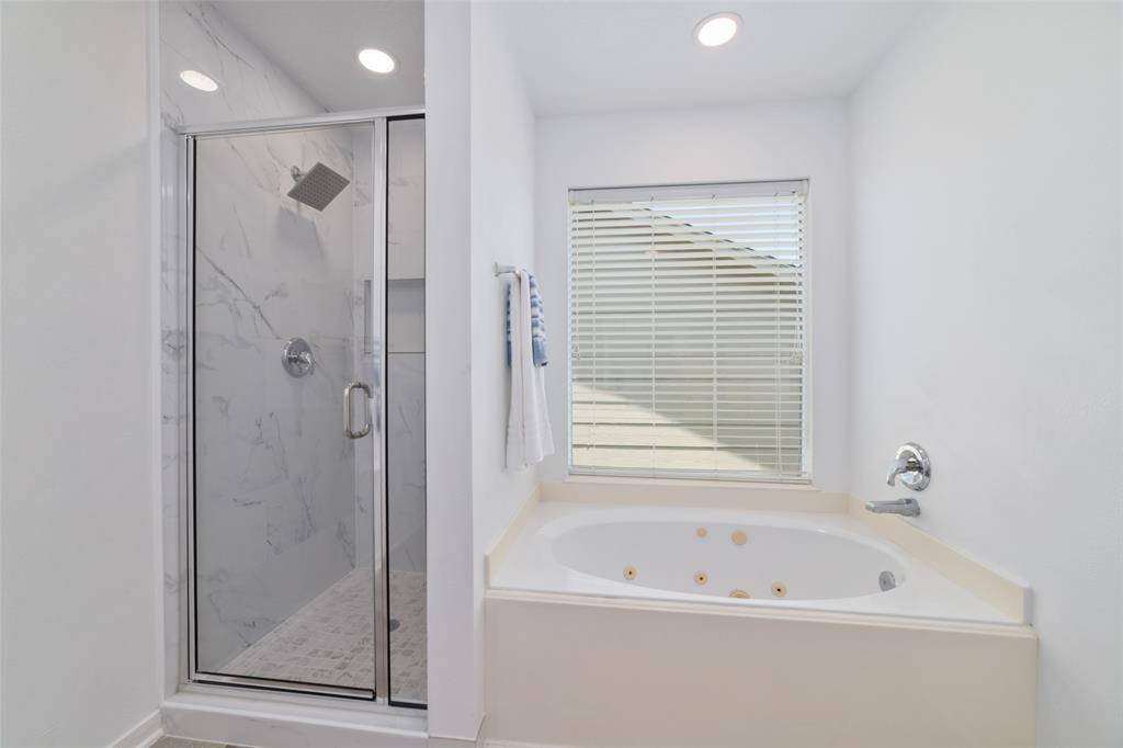 This bathroom features a modern glass-enclosed shower with marble-style tiles and a spacious jetted bathtub.