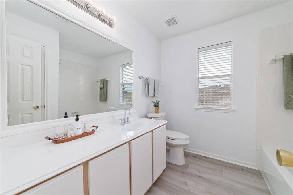 Bright and spacious bathroom featuring a large mirror, single sink, modern fixtures, and a bathtub.