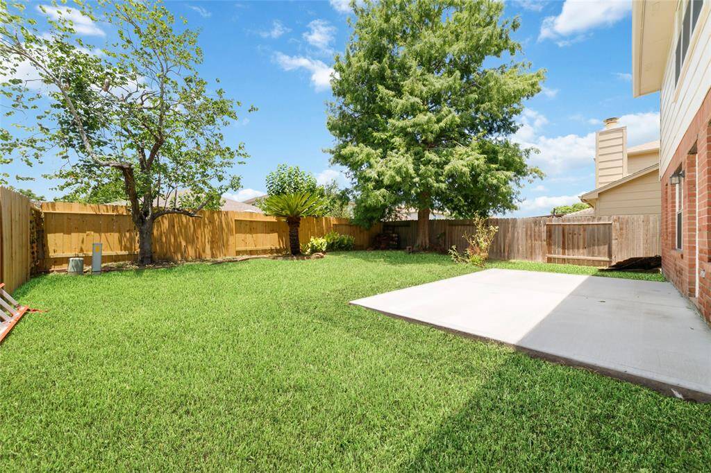 Spacious backyard with mature trees, and a concrete patio area, ideal for outdoor activities and relaxation. The yard is enclosed by a wooden fence, providing privacy.
