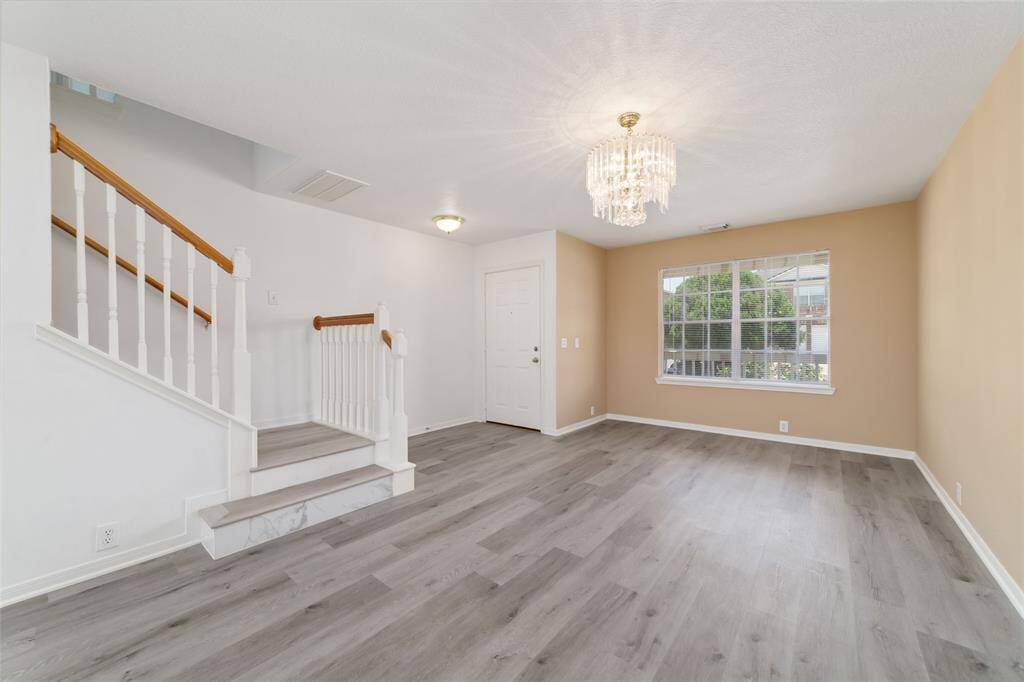 This bright living area features modern laminate flooring, a stylish chandelier, and an inviting staircase. The large window provides ample natural light.