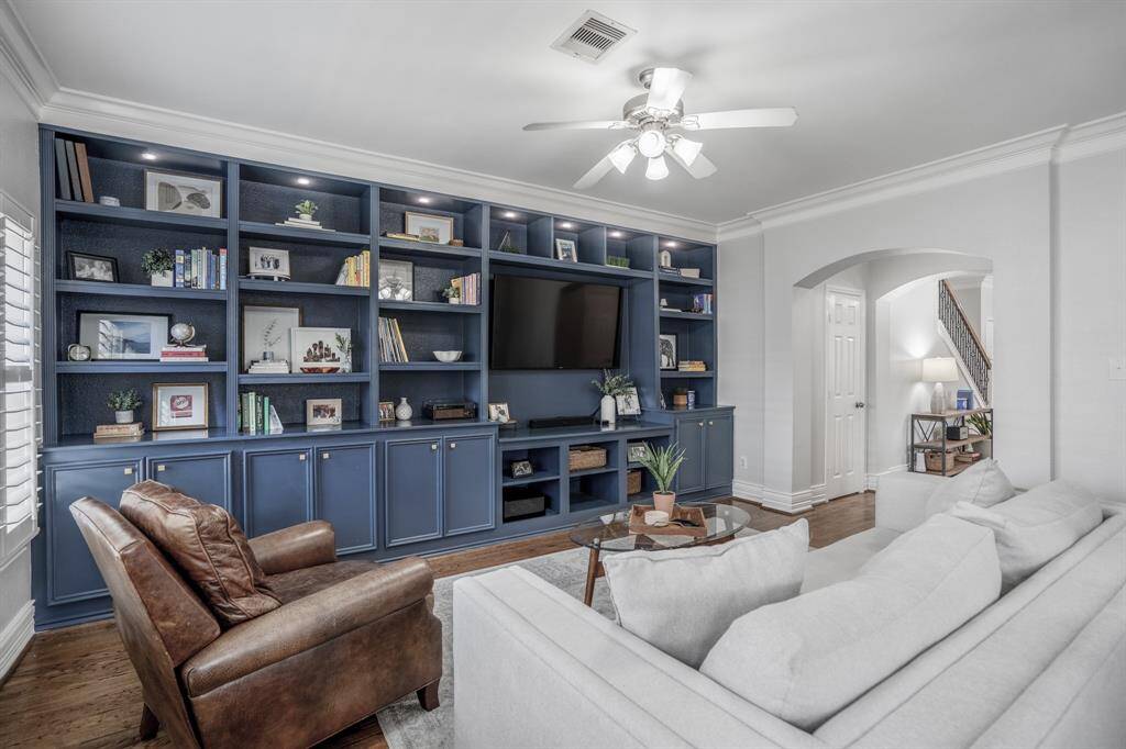 Further down the hallway, you'll stumble upon the spacious family room. Bold, custom built-ins in a moody blue hue add depth and personality to the living room, offering both smart storage and the perfect backdrop for your favorite reads, art, and collected treasures.