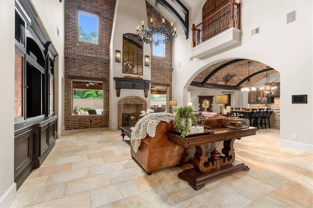 Grand two-story great room with beamed barrel ceiling, custom built-in entertainment center with sliding shelves, TV mount plus surround sound. The soaring fireplace with updated light fixtures is flanked by brick wall great backyard views, and impressive chandelier!