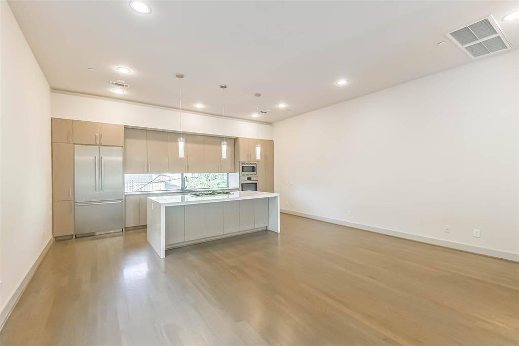 The sleek island kitchen features abundant storage, pendent accent lights, waterfall countertops and glass window backsplash.