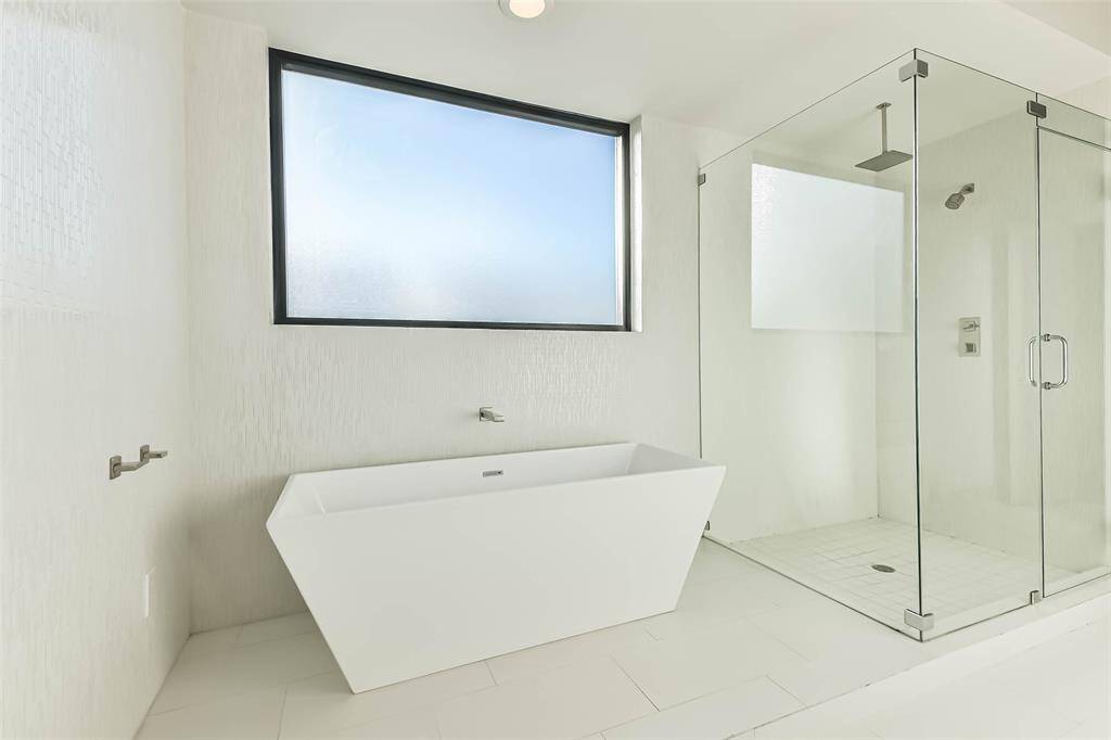 Primary bathroom with clean lines- features oversized soaking tub and an frameless glass shower with double shower heads.  The large window provides natural light creating a serene and relaxing ambiance.