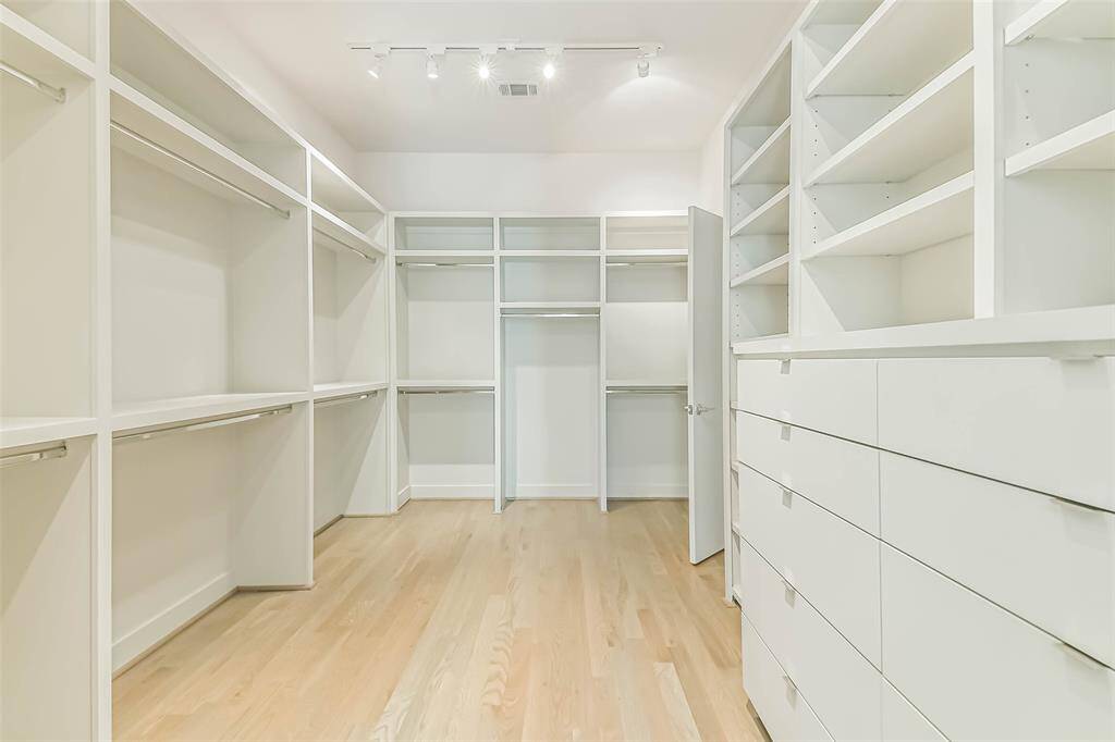 One of two Primary closets featuring custom built-ins to help stay organized.  Custom lighting & hardwood floors highlight the space.